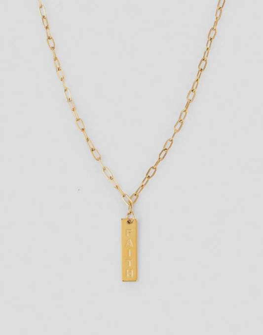 Gold necklace with a bar pendant with the word faith on a light gray background