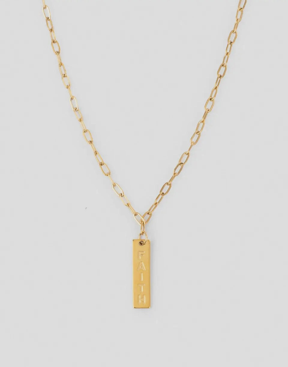 Gold necklace with a bar pendant with the word faith on a light gray background
