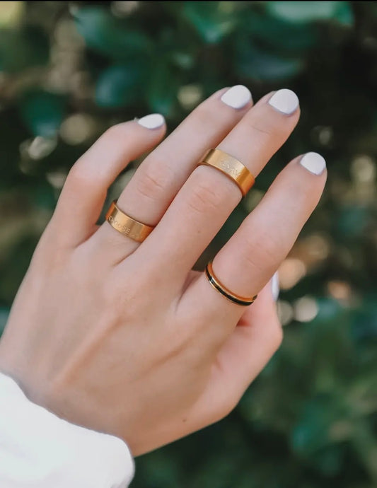 Hand wearing two gold rings with a blurred green background