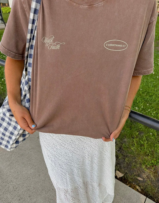 Person wearing a brown t-shirt with text and logos outdoors