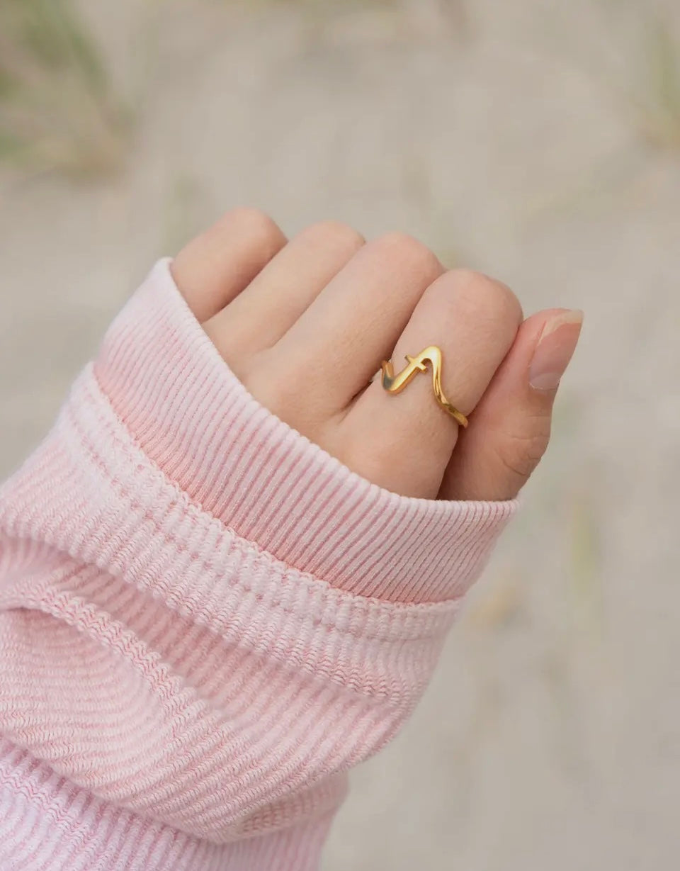Gold Wavy Cross ring on a finger with a blurred background