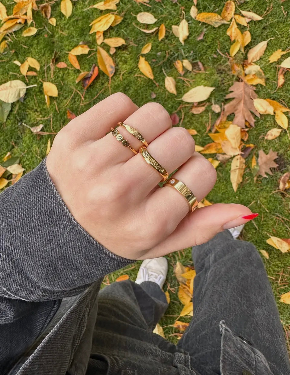Hand wearing gold rings on a grassy background with fallen leaves