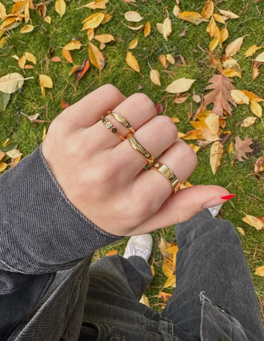 Hand wearing gold rings on a grassy background with fallen leaves